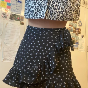 Svart blommig kjol med volang - Supersöt svart kort med små vita blommor och volangkant. Kjolen har knytband i midjan(dekoration) och en lätt, flowy känsla. Passformen är normal och tyget känns luftigt.