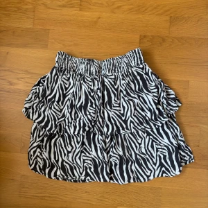 Zebramönstrad volangkjol - Supersöt kort kjol med zebramönster i svart och vitt. Kjolen har bred resår i midjan och volanger som ger en cool och lekfull look. Perfekt för dig som vill sticka ut lite extra. Skriv för fler bilder