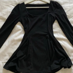 Svart långärmad topp med fyrkantig ringning - Snygg svart topp med lång ärm och en modern fyrkantig ringning. Modellen är lätt utsvängd nertill och sitter figurnära upptill. 