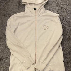 Vit hoodie från Hugo Boss med dragkedja - Vit hoodie från Hugo Boss med dragkedja framtill och huva. Diskret Boss-logga på bröstet och guldfärgad detalj på insidan av kragen. Mjuk bomullskänsla och klassisk passform, perfekt för en clean och stilren look.