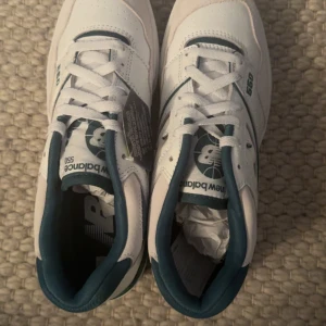 New Balance 550 vita och gröna sneakers - Snygga New Balance 550 sneakers i vitt skinn med gröna detaljer och logga. Klassisk retrodesign med rund tå, snörning och platt sula. Perfekta för dig som gillar streetstyle och vill ha en clean look med en sportig touch. Köpt i Sverige, oanvänd 