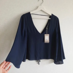 Mörkblå blus från Zara - Supersnygg mörkblå blus från zara med v-ringning och vida ärmar. Toppen har croppad passform och snörning framtill som ger en cool detalj. Tunt, lätt material som faller snyggt och känns luftigt. Perfekt att styla med jeans eller kjol.