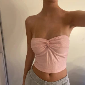 Ljusrosa ribbad bandeau tubtopp - Superfin ljusrosa bandeau tubtopp med twistad detalj framtill. Toppen är ribbad och sitter tight, perfekt för varma dagar. Mjuk och stretchig, passar snyggt till både jeans och kjol.