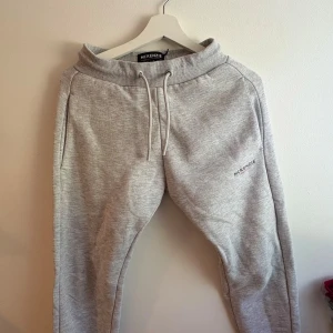 Grå mjukisbyxor från McKenzie - Snygga ljusgrå mjukisbyxor från McKenzie med broderad logga på benet. Byxorna har dragsko i midjan, ribbade muddar och två sidofickor. Perfekta för chill eller träning, tillverkade i mjukt bomullsmaterial för maximal komfort.