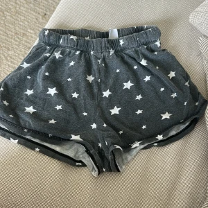 Mörkgrå shorts med stjärnor Seed Teen - Mysiga mörkgrå shorts från Seed Teen med vita stjärnor över hela tyget. De har elastisk midja och är perfekta för chill dagar hemma eller som pyjamasshorts. Tillverkade i mjuk bomull för extra komfort.