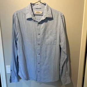 Ljusblå linneskjorta från Dressmann - Snygg ljusblå skjorta från Dressmann i mjukt linne. Klassisk krage, bröstficka och knappar framtill. Perfekt för dig som gillar en avslappnad men stilren look. Långärmad och passar till många olika outfits.