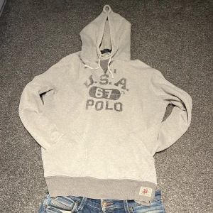 Grå hoodie från Ralph Lauren - Snygg grå hoodie från Polo Ralph Lauren med tryck 'U.S.A. 67 POLO' på bröstet. Hoodien är i storlek L men passar även M. Pris kan diskuteras!! Hör av dig vid frågor!