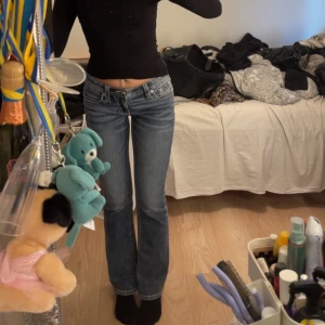 Miss Me blå bootcut jeans med broderi - Snygga blå jeans från Miss Me med låg midja och bootcut passform. Jeansen har coola broderade detaljer och bling på bakfickorna samt slitningar och kontrastsömmar. Perfekta för dig som vill sticka ut med en unik denimstil. storlek 26