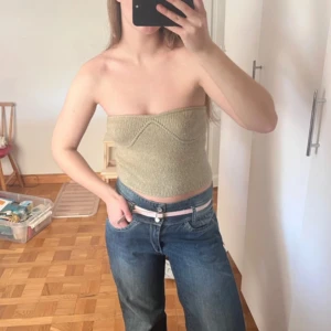 Beige stickad bandeau tubtopp - Säljer en beige stickad bandeau tubtopp med markerad söm över bysten. Toppen är ärmlös och croppad, perfekt för varma dagar. Materialmix med polyester, nylon, alpacka och elastan för en mjuk och stretchig känsla.