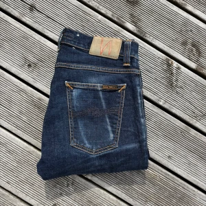 Mörkblå ”Tight Terry” jeans från Nudie - Snygga mörkblå jeans från Nudie med klassiska orange sömmar. Jeansen har fem fickor, läderpatch med Nudie-logga och coola slitningar på benen. Tillverkade i mjukt och slitstarkt bomullsmaterial som sitter tajt och bekvämt. Kom gärna med frågor!🙌 W30 L32