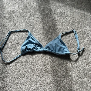 Ljusblå trekantsbikini  - Snygg ljusblå trekantsbikini med justerbara axelband. Klassisk modell med slät yta och tunna band, perfekt för strandhäng. Insidan är vit och materialet känns mjukt och följsamt mot huden.