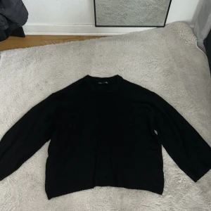 Svart stickad tröja från 157 - Svart stickad tröja från 157 i storlek M. Tröjan har en enkel och clean design med rund hals och långa ärmar. Passformen är loose och den är perfekt för att chilla eller hänga med kompisar. Materialet är mjukt och känns skönt mot huden.