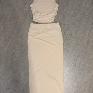 Beige långklänning - Supersnygg beige långklänning med croppad överdel och rynkade sidor. Klänningen har ärmlös design och sitter jätte fint på kroppen. Den är inte genomskinlig alls. Priset kan diskuteras!!