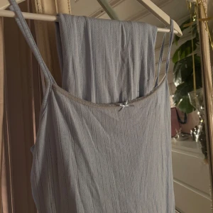 Ljusblå långkjol inklusive topp med spetsdetalj - Supersöt ljusblå långkjol inklusive topp med tunna axelband och liten rosett framtill. Det har ett supersött ribbat mönster i tyget och är perfekt för varma dagar. Materialet känns mjukt och luftigt. Långkjolen är i storlek L och toppen i storlek XL. Spetsen på toppen är lite urtvättat!