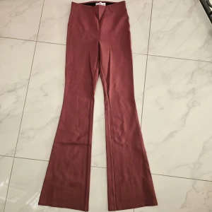 Mörkröda bootcut byxor - Snygga mörkröda bootcut byxor med hög midja och utsvängda ben. Byxorna har en stilren look och är tillverkade i ett mjukt bomullsmaterial som känns skönt mot huden. Perfekta för dig som vill ha en trendig siluett och sticka ut med färg.
