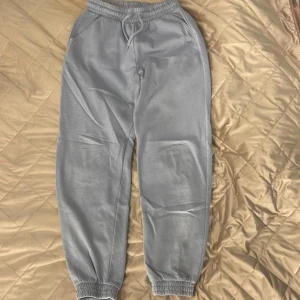 Ljusgrå mjukisbyxor från Lindex - Säljer ett par ljusgrå mjukisbyxor från Lindex med trycket 'TODAY TOMORROW' på benet. Byxorna har elastisk midja med snörning, ribbade muddar vid benslut och är gjorda i mjuk bomull. Perfekta för chill dagar eller träning.