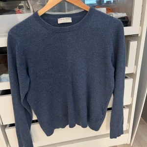 Blå stickad tröja från Tiger of Sweden - Snygg blå stickad tröja från Tiger of Sweden med rund hals och långa ärmar. Enkel och stilren design som passar perfekt till jeans eller chinos. Mjuk och skön kvalitet, perfekt för kyliga dagar. Klassisk modell med ribbade muddar vid hals, ärmslut och nederkant. Passar mig som bär strl. XS-S