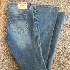 Flared jeans true religion - Supersnygga flared low waisted jeans från True Religion, med rosa brodyr! Säljer för att de är för långa för mig, endast använda en gång men har en liten skada längst ner på ena byxbenet (se sista bilden) annars toppenskick! Storlek W26🩷Nypris 1400