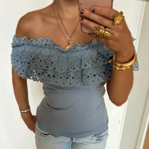 Ljusblå offshoulder topp med volang - Supersöt ljusblå offshoulder topp med breda volanger och broderade spetsdetaljer. Sitter tight över kroppen och har en romantisk vibe med sin dubbla volangkant. 