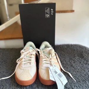 Adidas VL Court 3.0 sneakers ljusrosa - Fräscha Adidas VL Court 3.0 sneakers i ljusbeige och ljusrosa med klassiska tre ränder på sidan. Skorna har en platt gummibrun sula och snörning framtill. Ovandelen är i syntet och mocka, med mjuk mintgrön insida för extra komfort. Perfekt för dig som gillar clean och sportig stil. De är sprillans nya, helt oanvända och väldigt fint skick. Boxen och kvitto finns vid behov av att se de. Köpte för 780kr mitt pris 699kr. Lägg bud som kan diskuteras. Det är bara att höra av sig vid minsta fundering.