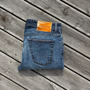 Blå jeans från Jacob Cohën - Snygga blå jeans från Jacob Cohën med klassisk femficksdesign och orange patch med logga bak. Jeansen har raka ben och gröna sömmar på bakfickorna som ger en unik touch. Perfekt för dig som gillar stilrena och coola jeans med exklusiv känsla. ‼️Omsydda ner till så passar bäst någon som är mellan 170-175 cm‼️Har även några ställen där defekter är sydda! Kan gå ner i pris vid snabbaffär 🤝
