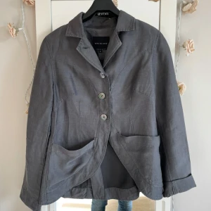 Grå kavaj från Bitte Kai Rand - Snygg vintage grå kavaj från Bitte Kai Rand i storlek S. Jackan har klassisk krage, tre knappar framtill och två stora fickor. Materialet är linne  passformen är normal. Perfekt för dig som gillar stilrena och tidlösa plagg.