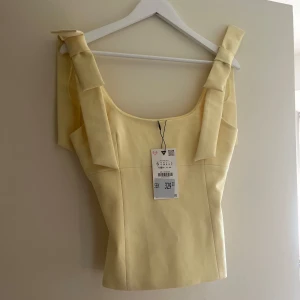 Gul linnetopp med rosett-detaljer - Supersöt ljusgul linnetopp från Zara med breda axelband och snygga rosetter på axlarna. Helt oanvänd med prislapp kvar💛💛 