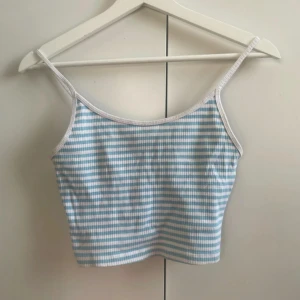 Randig ljusblå linnetopp FB Sister - Supersöt croppad linnetopp från FB Sister i storlek S. Toppen har tunna axelband och är randig i ljusblått och vitt med vit kant runtom. Perfekt för varma dagar och chill outfits. Materialet är mjukt och toppen är kortare vid magen.
