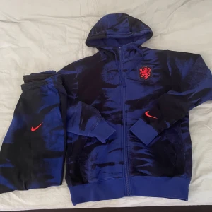 Nike tracksuit - Snygg tracksuit från Nike  ”Nederländerna” i blått och svart med coolt mönster och röd logga på bröstet.  Perfekt för dig som gillar sportig stil och vill sticka ut med ett unikt plagg.