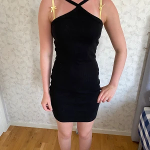 Svart ribbad kortklänning 157 XS - Supersnygg svart ribbad klänning från 157 i storlek XS. Modellen är kort med tight passform och har smala axelband som korsas framtill. Perfekt för dig som gillar minimalistisk stil med en twist. Materialet är mjukt och stretchigt, vilket gör den bekväm att bära hela dagen.