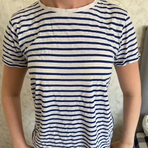 Randig t-shirt från New yorker - Snygg vit t-shirt med blå horisontella ränder från New yorker. Modellen är klassisk med rund hals och korta ärmar. Tillverkad i mjuk bomull som känns skön mot huden. Perfekt för dig som gillar en enkel och fräsch stil med lite marint vibe.