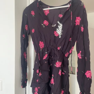 Blommig kortklänning från Motel - Supersöt kortklänning från Motel. Klänningen har v-ringning, långa ärmar med smock vid handlederna och volangdetaljer. 