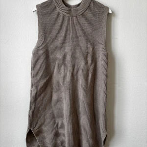 Beige stickad väst från H&M - Säljer en beige stickad väst från H&M i storlek M. Västen har en ribbad struktur, hög hals och är ärmlös med slitsar på sidorna. Materialet är 60% bomull och 40% akryl, vilket gör den både mjuk och lite chunky. Perfekt att styla över en skjorta eller t-shirt.