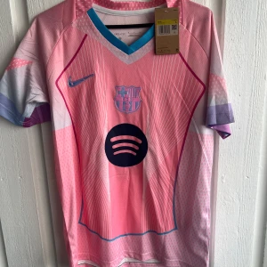 Barça Lamine Yamal rosa matchtröja - Snygg FC Barcelona fotbollströja med Lamine Yamal och nummer 10 på ryggen. Tröjan är rosa med vita och lila detaljer, har korta ärmar och coolt mönster med tunna linjer. Spotify-logga på bröstet och UEFA Foundation-märke på ärmen. Perfekt för dig som älskar Barça!