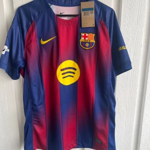 Barcelona matchtröja Roony 19 Nike - Snygg FC Barcelona matchtröja med Roony och nummer 19 på ryggen. Tröjan är randig i blått och rött med gula detaljer, klubbmärke och sponsortryck. Kortärmad modell i lätt och ventilerande material, perfekt för fotboll eller häng med kompisar.