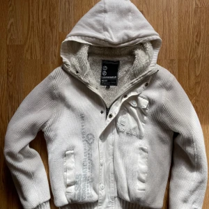 Hoddie från  Crosshatch - Säljer en vit teddyjacka från Crosshatch med huva och mysigt fluffigt foder. Jackan har stickad utsida, dragkedja och knappar framtill, samt en cool bröstficka med knapp. Perfekt för kalla dagar och har en chill streetstil.