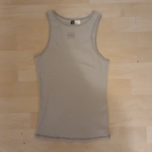 Ljusgrå ribbad linnetopp  - Säljer en ljusgrå ribbad linnetopp från H&M. Toppen är ärmlös och har ett litet tryck framtill på linnet. Väldigt simpel och passar bra med t.ex jeans. Har aldrig använt och har prislapp kvar. 💖