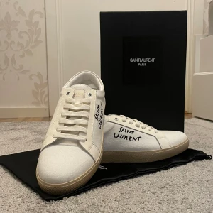 Saint Laurent vita sneakers - Snygga vita sneakers från Saint Laurent med handskriven logga på sidan. Skorna har rund tå, platt sula i beige och klassisk snörning. Ovandelen är i slät skinn och textil, vilket ger en clean och lyxig vibe. Perfekta för dig som gillar stilrena designer med exklusiv känsla. Pris kan diskuteras 