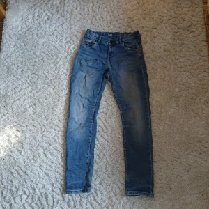 Blå relaxed fit jeans från LAB Industries storlek 170 - Snygga blå jeans från LAB Industries i modellen Eddy Relaxed Fit. Jeansen har klassisk femficksdesign, normal passform och är tillverkade i hållbar denim. De har en lätt tvättad look med subtila slitningar och raka ben. Perfekt för dig som gillar avslappnad stil.