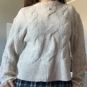 Beige stickad kabeltröja - Mysig beige stickad tröja med grovt kabelmönster framtill och på ärmarna. Tröjan har rund hals och långa ärmar med ribbade muddar. Perfekt för kyliga dagar när du vill vara både bekväm och snygg. Storlek 146/152 men passar mig som har xxs/xs