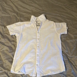 Vit kortärmad skjorta Jack & Jones XS - Fräsch vit skjorta från Jack & Jones Essentials, modell 'The Summer Shirt'. Skjortan har klassisk krage, korta ärmar och knappar framtill. Tillverkad i en skön mix av bomull och linne som känns lätt och luftig. Perfekt för varma dagar och enkel att styla.