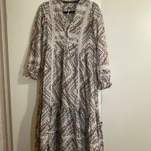 Odd Molly långklänning med spets - Säljer en boho-inspirerad långklänning från Odd Molly med blommigt mönster i beige, svart och vinrött. Klänningen har v-ringning, spetsdetaljer och långa ärmar med resår vid ärmslut. Tillverkad i mjuk bomull, perfekt för dig som gillar avslappnad och cool stil.