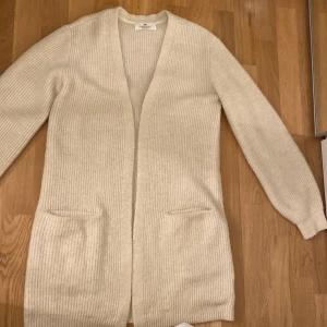 Ribbad beige kofta från H&M - Säljer en lång, ribbad beige kofta från H&M i storlek 158/164. Koftan har två fickor framtill, långärmad design och öppen framtill utan knappar. Perfekt att slänga över en t-shirt för en chill look.