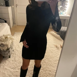 Svartglittrig klänning - Säljer nu denna superfina svartglittrig ribbade klänning med långärmade, lätt utsvängda ärmar och rund hals. Klänningen är kort och har en söt kantdetalj längst ner. Passformen är slim och materialet känns mjukt och stretchigt, perfekt för dig som gillar stilrena och enkla plagg. Använd fåtal gånger.