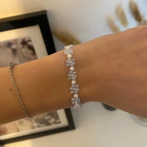 Pärlarmband med blommor i vitt och blått - Supergulligt egentillverkat armband med små blommor av ljusblå pärlor och vita pärlor i mitten. Armbandet har en silverfärgad kedja och lås🩵