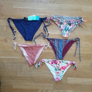 Fem snygga bikiniunderdelar i olika färger - Fem bikiniunderdelar säljes! En marinblå med snörning och pärldetaljer, en ljusrosa med knyt i sidorna, en blommig med leopardmönster och volang, en mönstrad i vinrött och blått med snörning, samt en vit med färgglatt blommönster och knyt. I storlek 36-38