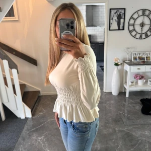 Vit blus med  volang - Supersöt vit blus med långärmade ärmar och volang nertill. Blusen är använd ett fåtal gånger och är i väldigt bra skick. Skriv om ni är intresserade av fler bilder