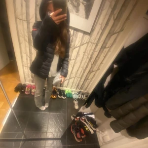 Svart pufferjacka med huva - Säljer en svart pufferjacka med huva och dragkedja framtill. Jackan har quiltad design och två sidofickor med dragkedja. Perfekt för dig som vill ha en stilren och varm jacka med snygg passform. Passar dig som gillar streetstyle och enkel look.