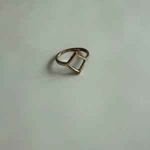 Guldfärgad ring med geometrisk design - Minimalistisk ring i guldfärg med en öppen fyrkantig form framtill. Snygg och stilren, perfekt för dig som gillar enkla och moderna smycken. Den tunna ringen har en unik geometrisk look som sticker ut utan att ta över.
