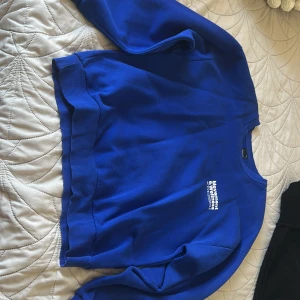 Blå sweatshirt från Gina Tricot - Blå sweatshirt från Gina Tricot med vit text på bröstet. Tröjan har rund hals, ribbade muddar och är tillverkad i mjuk bomullsmix. 